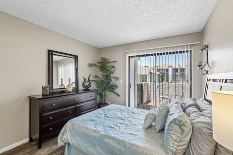 A bedroom with a bed, dresser, mirror, and a plant.