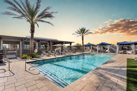 A large swimming pool surrounded by a patio area with lounge chairs and umbrellas.