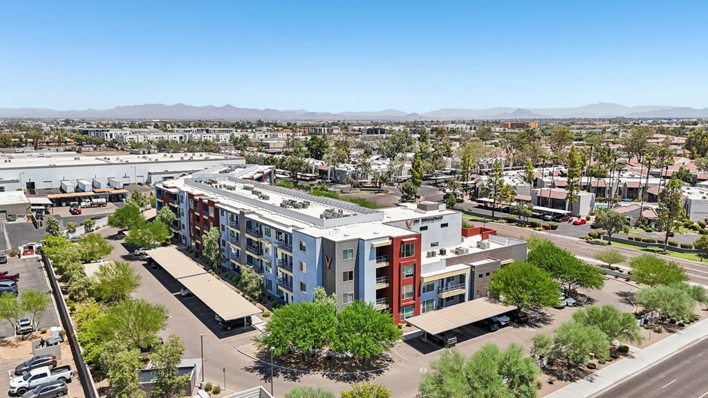 A large building with a red section is surrounded by trees and other buildings.