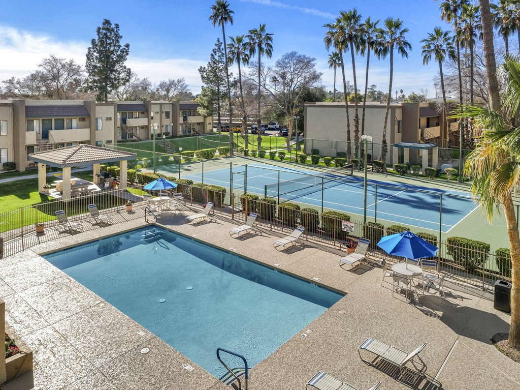 A pool surrounded by palm trees and a tennis court.