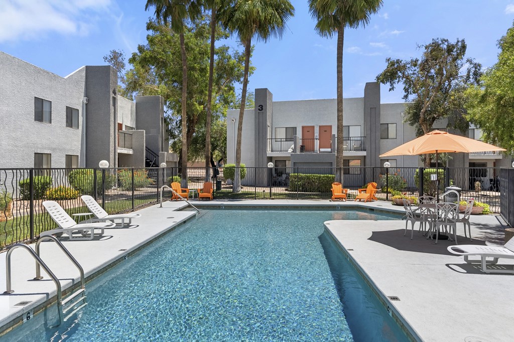 A swimming pool surrounded by chairs and trees in front of a building.