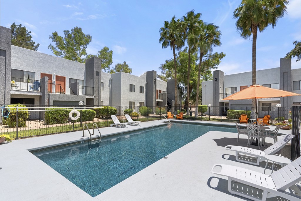 A swimming pool surrounded by lounge chairs and umbrellas in a sunny outdoor setting.