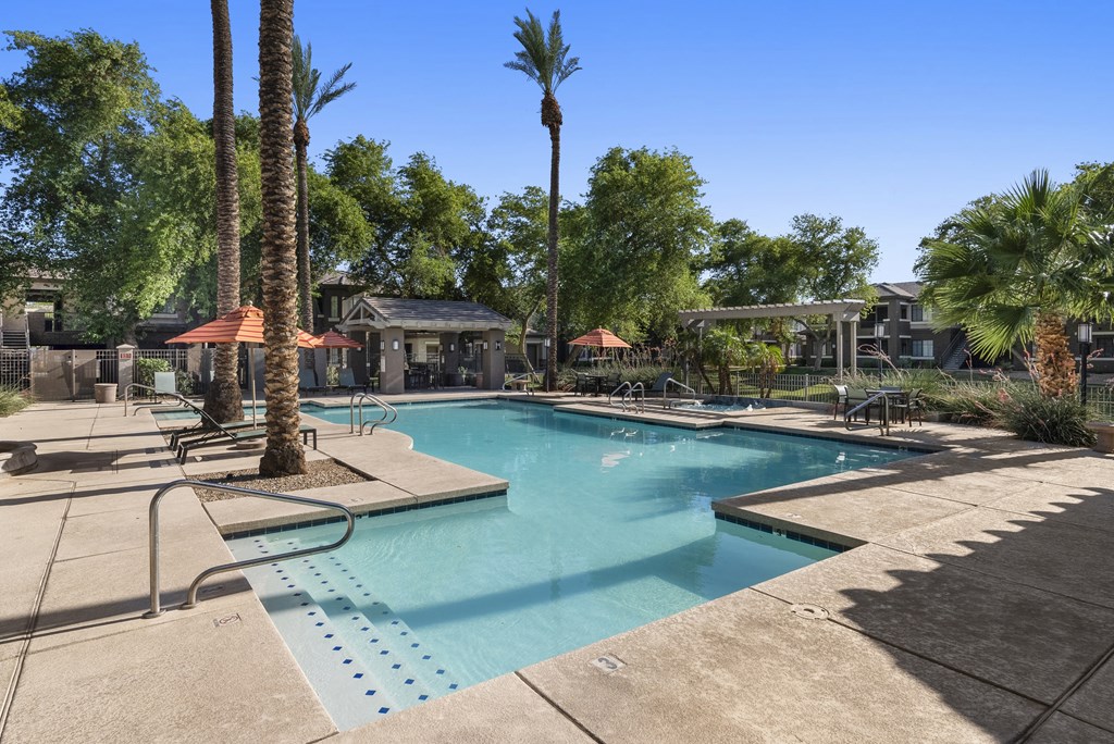 A pool surrounded by palm trees and a building in the background.