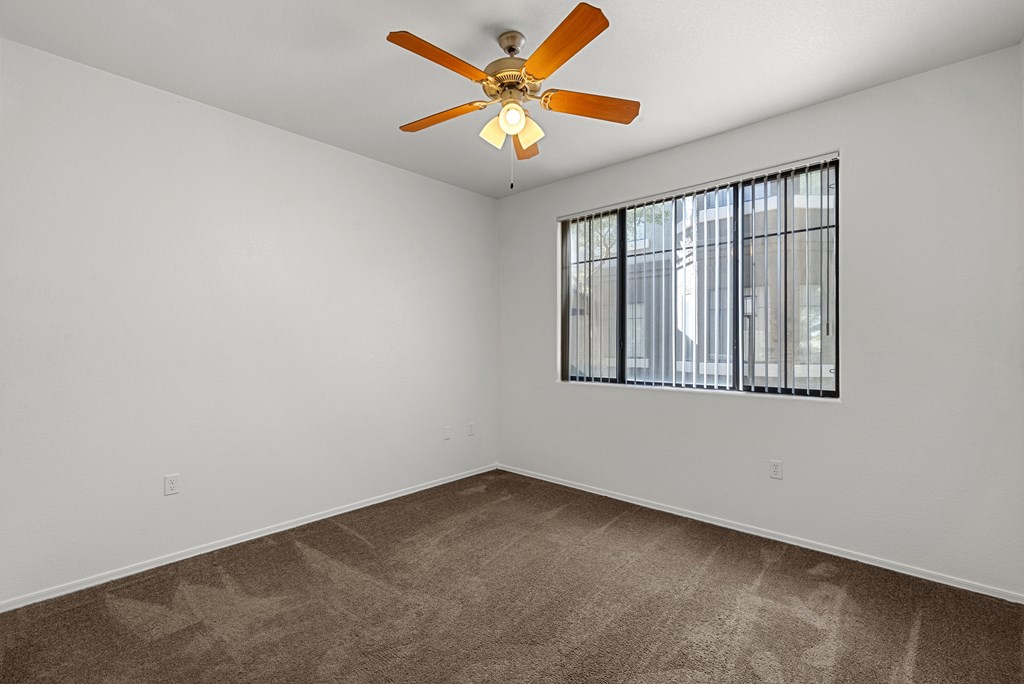 Empty room with a ceiling fan and a window with bars.
