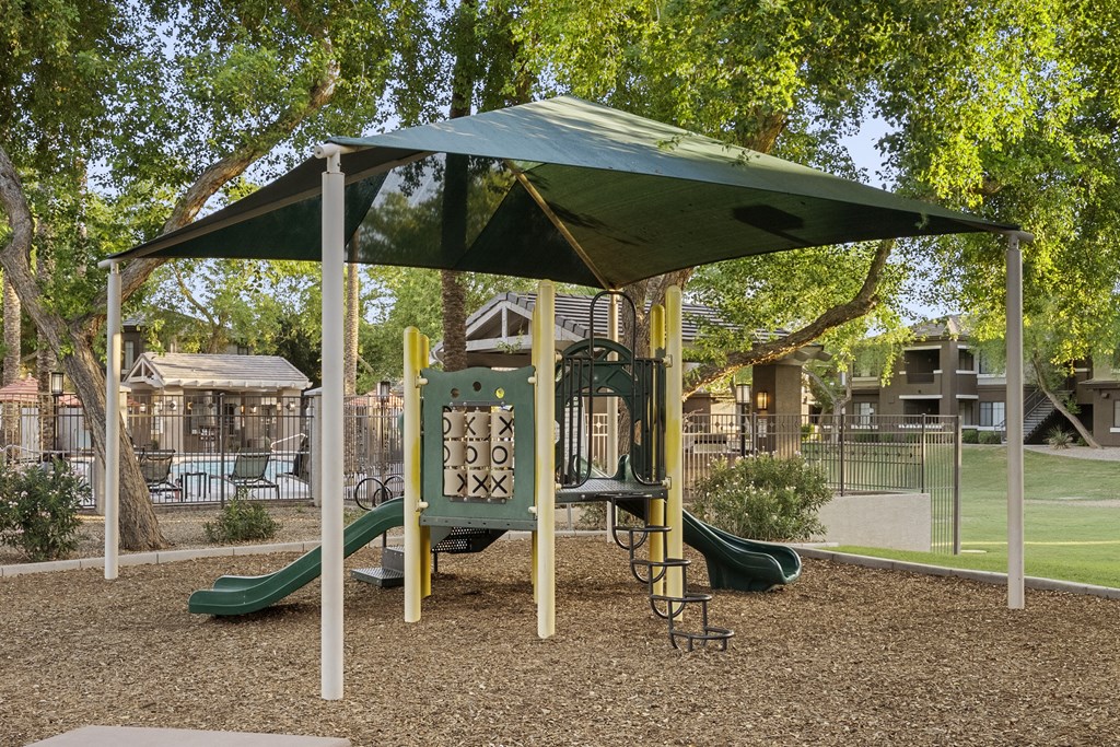 A playground with a green slide and a canopy.