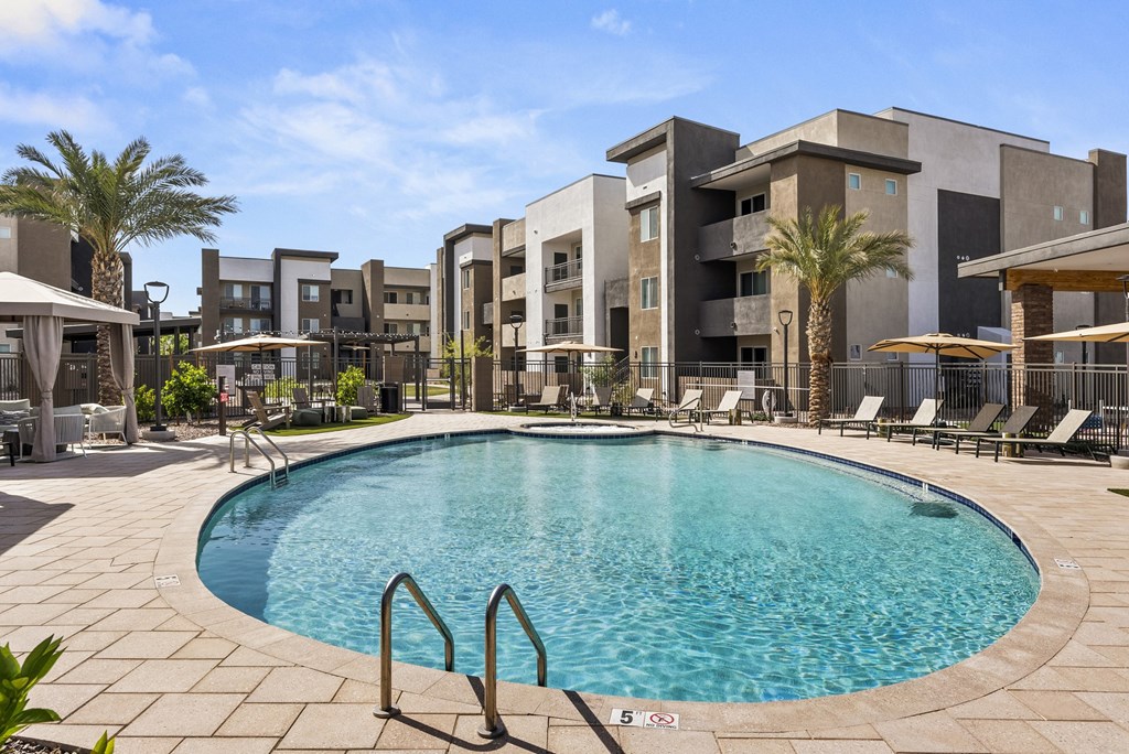 A swimming pool surrounded by lounge chairs and umbrellas in front of a modern building.