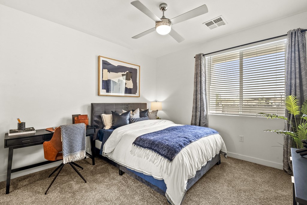 A bedroom with a bed, desk, chair, and a ceiling fan.