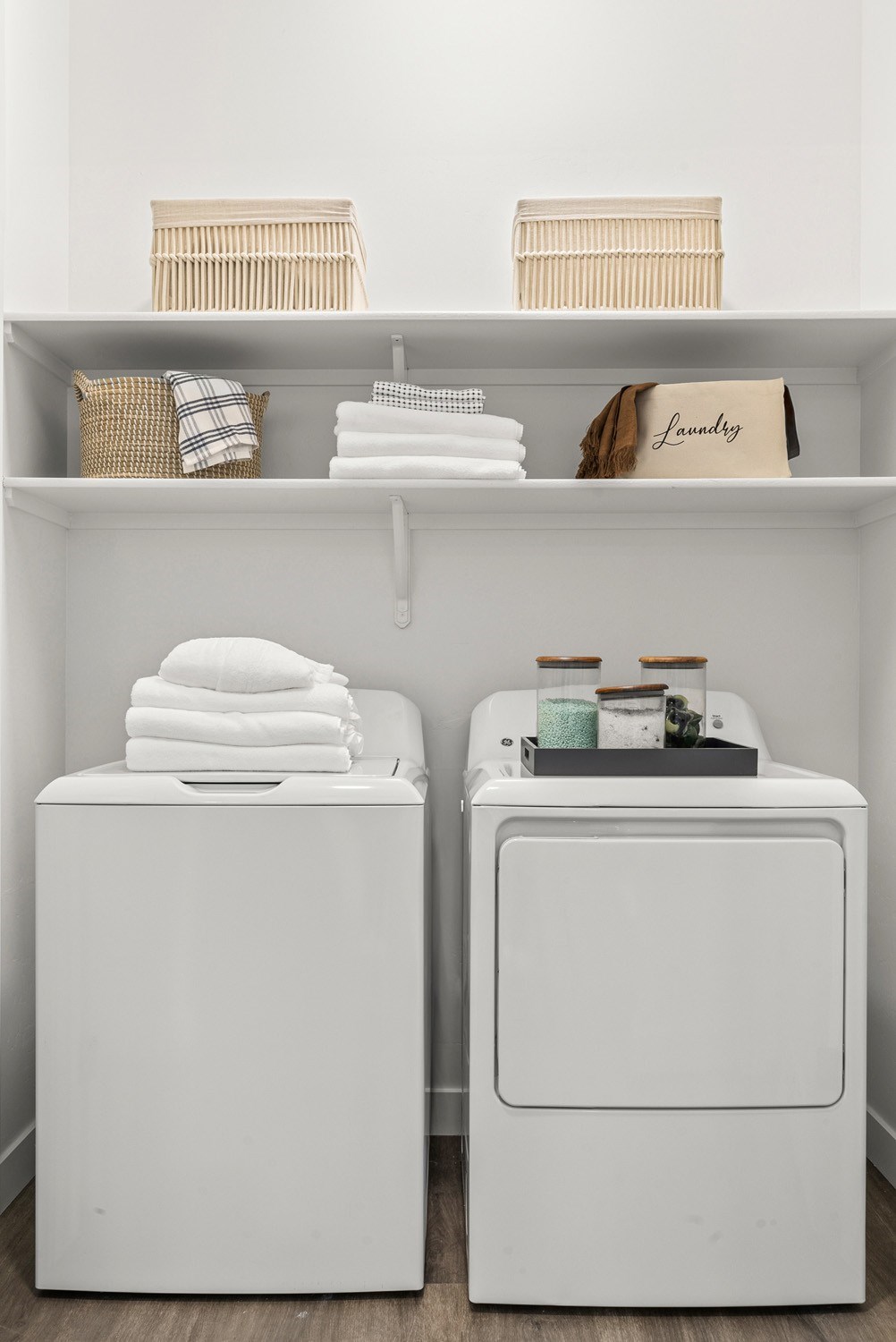 Two white washing machines with towels and baskets on top.