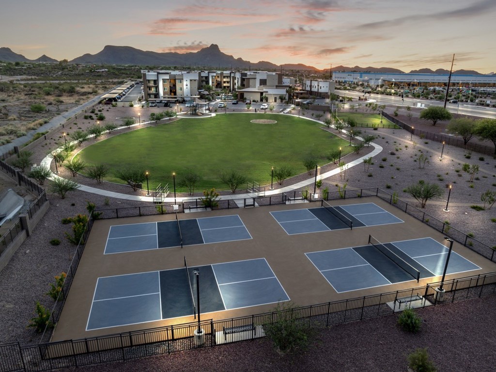 Tennis courts are surrounded by a grassy area and a building in the background.