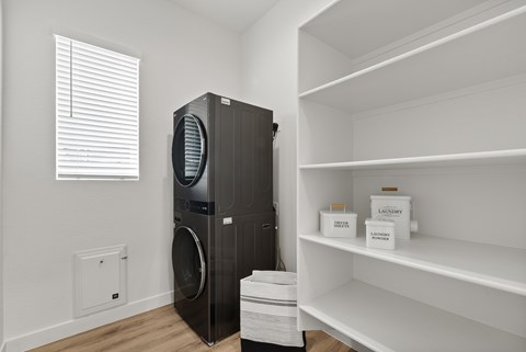 A black dryer is in a laundry room with a white wall and a window.