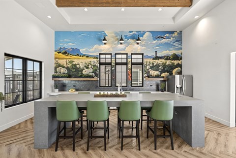 A kitchen with a large mural on the wall and green chairs.