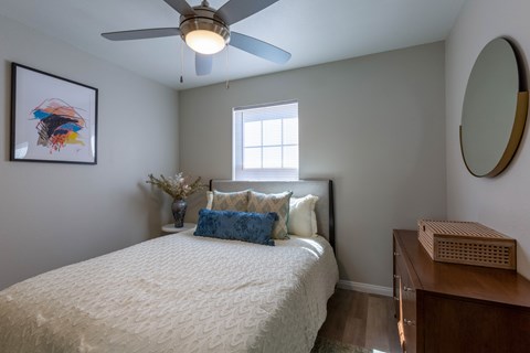 A bedroom with a bed, a ceiling fan, and a mirror on the wall.