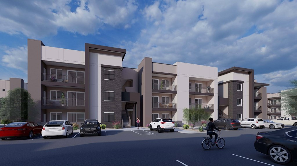 A modern apartment complex with cars parked in front and a person riding a bicycle.