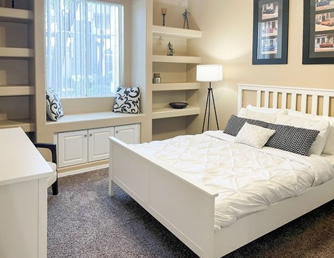 A white bed with a white comforter and pillows in a bedroom with a window.