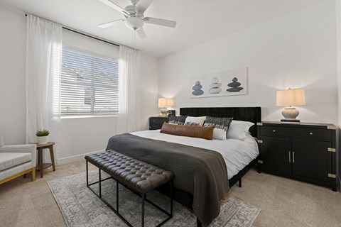 A bedroom with a large bed, a bench, and a ceiling fan.