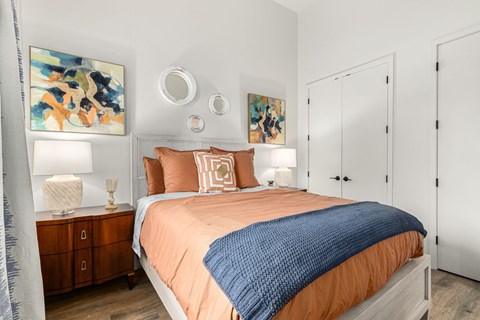 A bedroom with a bed, nightstand, and two pieces of artwork on the wall.