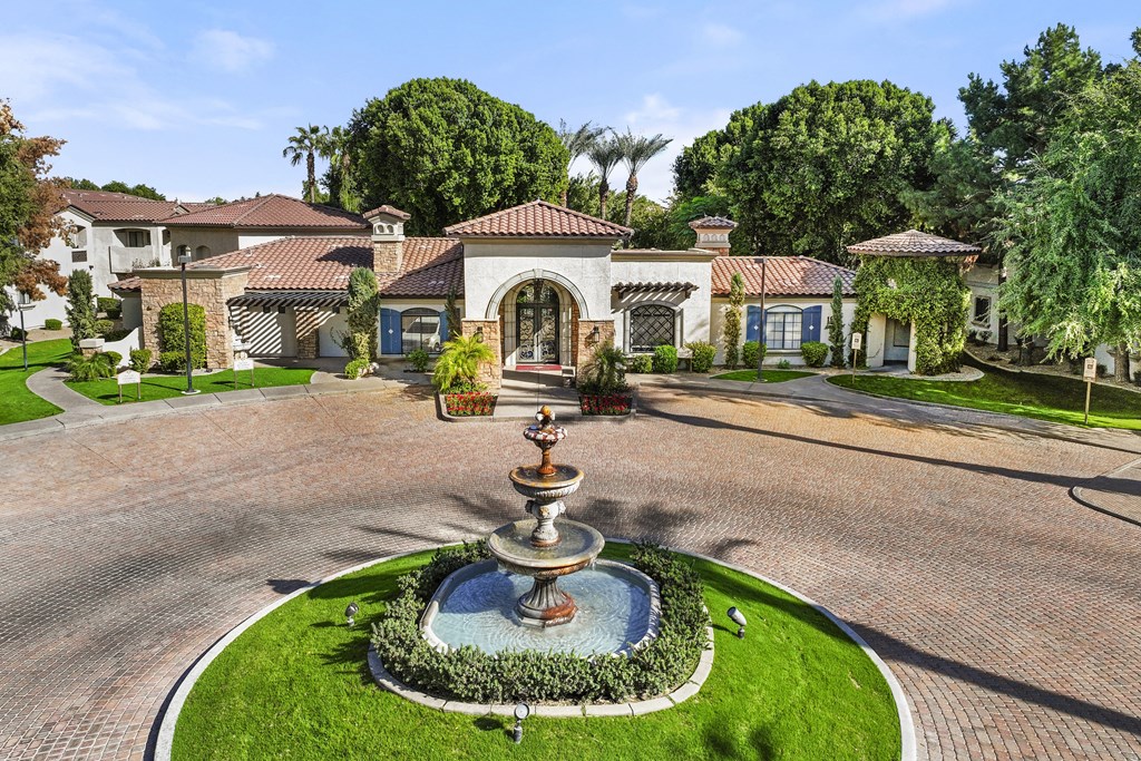 A fountain in the middle of a paved area with a house in the background.
