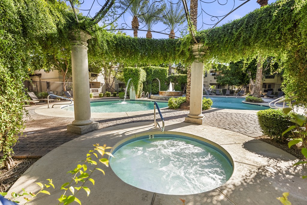 A hot tub sits in the middle of a patio under a vine covered pergola.
