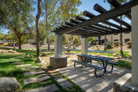 A picnic table is under a pergola in a park.