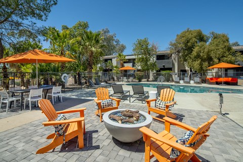 A patio with orange chairs and a fire pit.