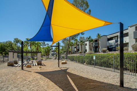 A playground with a blue and yellow shade structure.