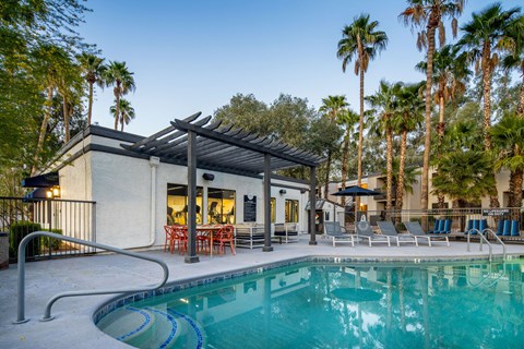 A pool in front of a house with a patio and palm trees.