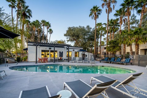 A pool with lounge chairs and a house with a patio.