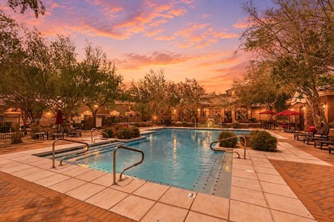 A swimming pool surrounded by trees and lounge chairs at sunset.