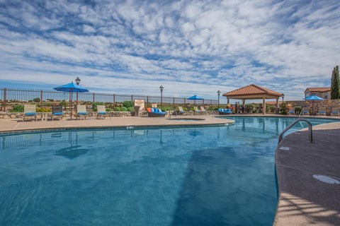 A large outdoor swimming pool with a blue sky and clouds in the background.