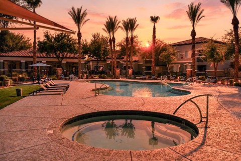 A swimming pool surrounded by palm trees at sunset.