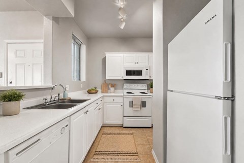 A white kitchen with a sink, stove, and refrigerator.