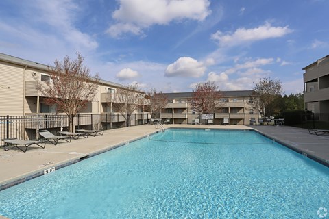 A large swimming pool in front of a building with trees and a blue sky.