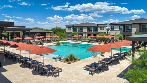 A pool surrounded by chairs and umbrellas with apartment buildings in the background.