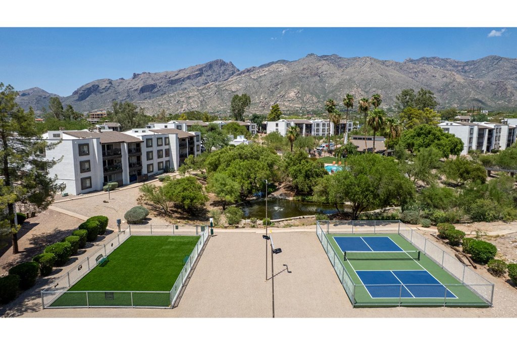 A tennis court is surrounded by a green lawn and apartment buildings.