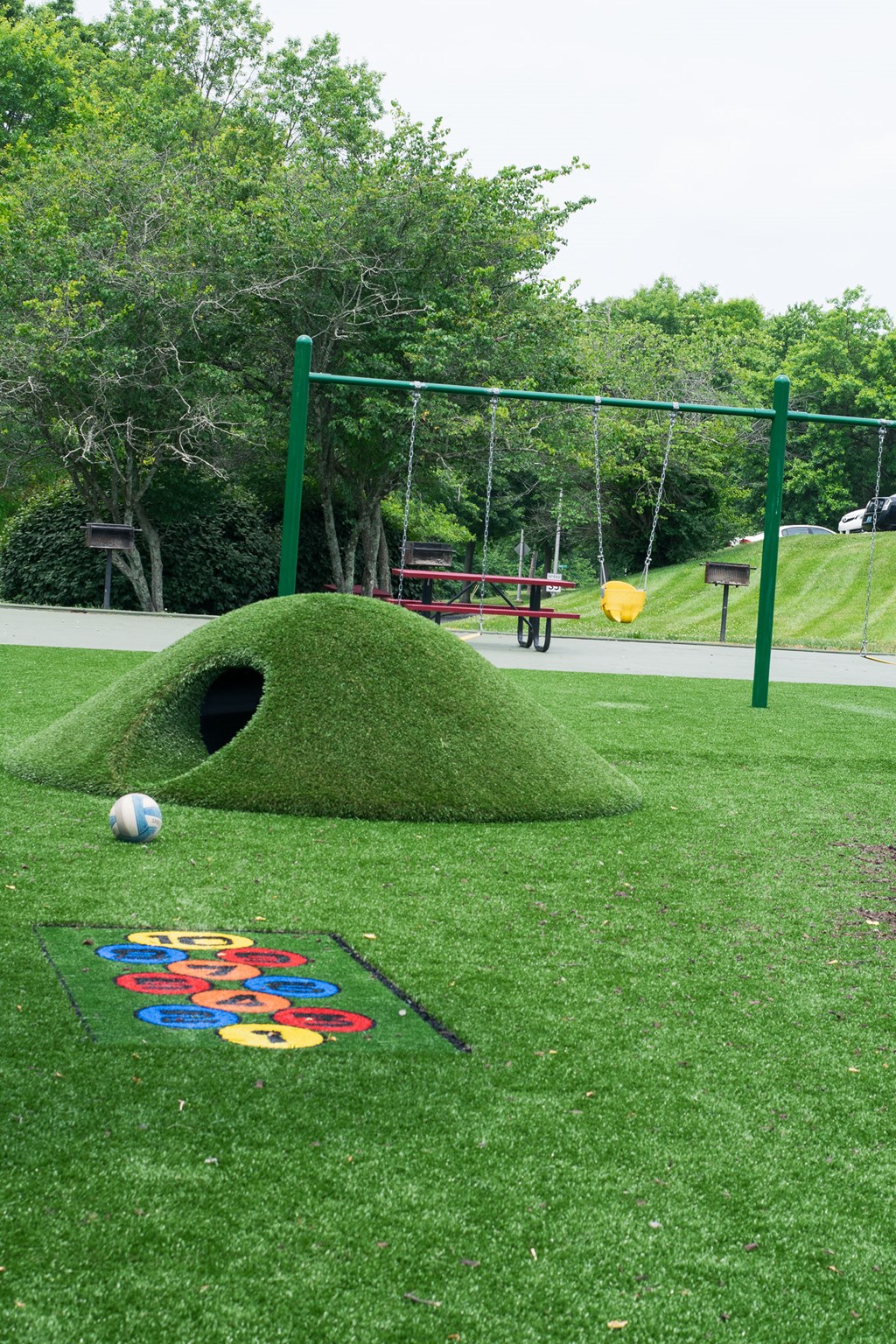A playground with a green swing set and a ball on the ground.