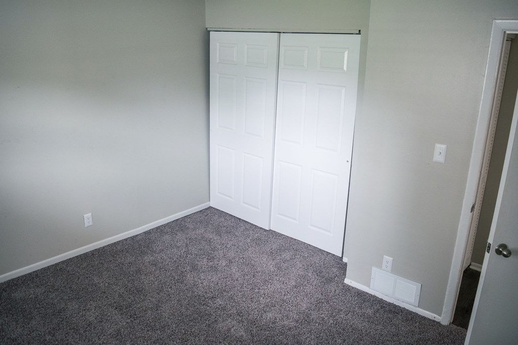 A room with a white door and grey carpet.