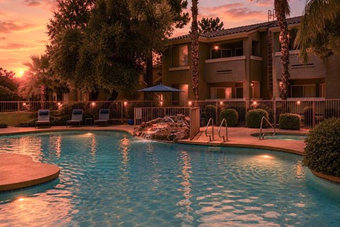 A pool surrounded by a fence and trees with a sunset in the background.