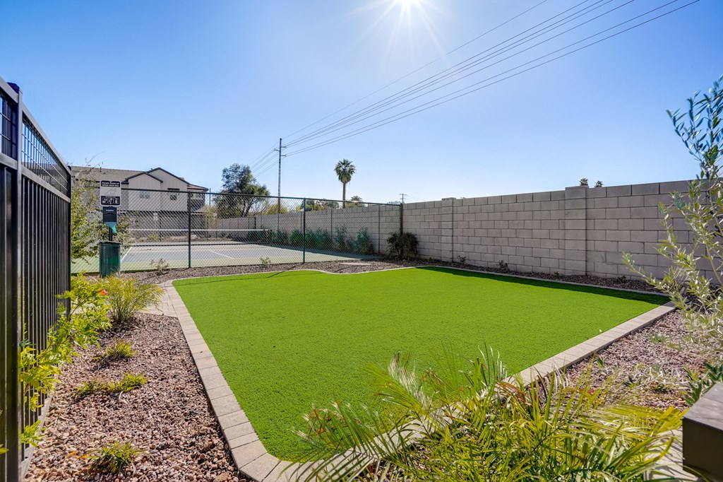 a backyard with a lawn and a fence and a tennis court