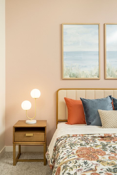 A bedroom with a bed, a nightstand with a lamp, and two pictures on the wall.