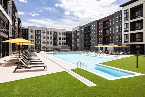A swimming pool surrounded by lounge chairs and umbrellas in a courtyard.