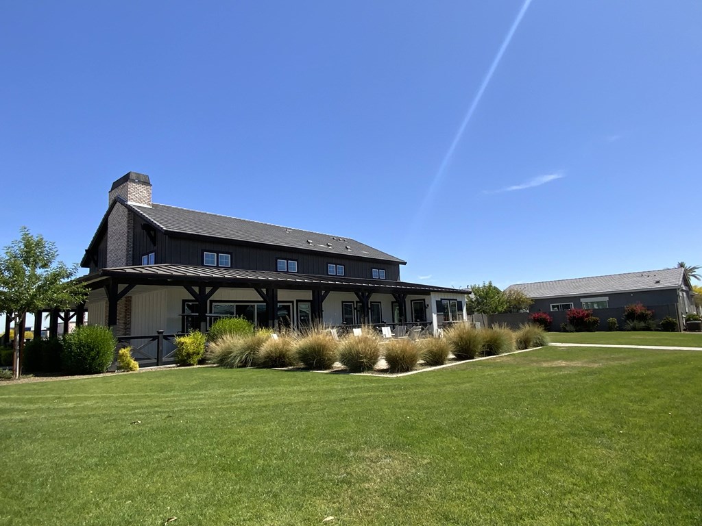 A large building with a black roof and white walls is surrounded by a grassy area and some bushes.