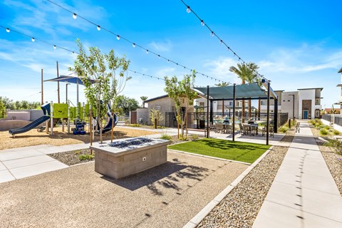 A playground with a slide, swings, and a tree in a sunny park.