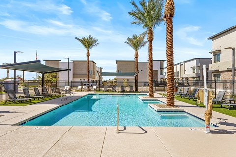 A pool surrounded by palm trees and a building in the background.