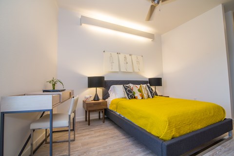 A bedroom with a bed, desk, chair, and a ceiling fan.