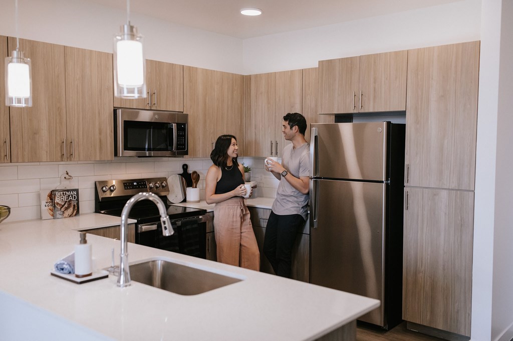 Two people standing in a kitchen with a sink and refrigerator.