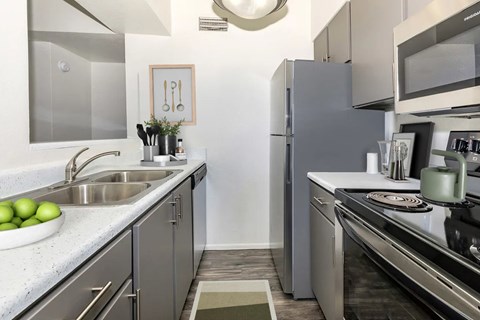 A modern kitchen with a stainless steel refrigerator and a sink with a bowl of green apples on the counter.