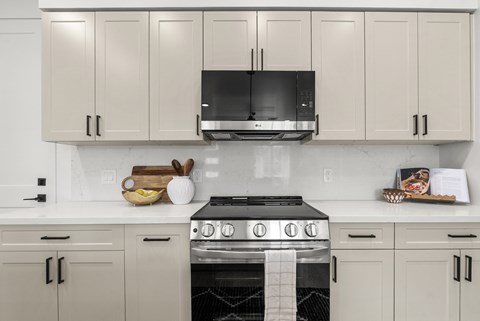 A kitchen with a black microwave above a stove with a white towel draped over the front.