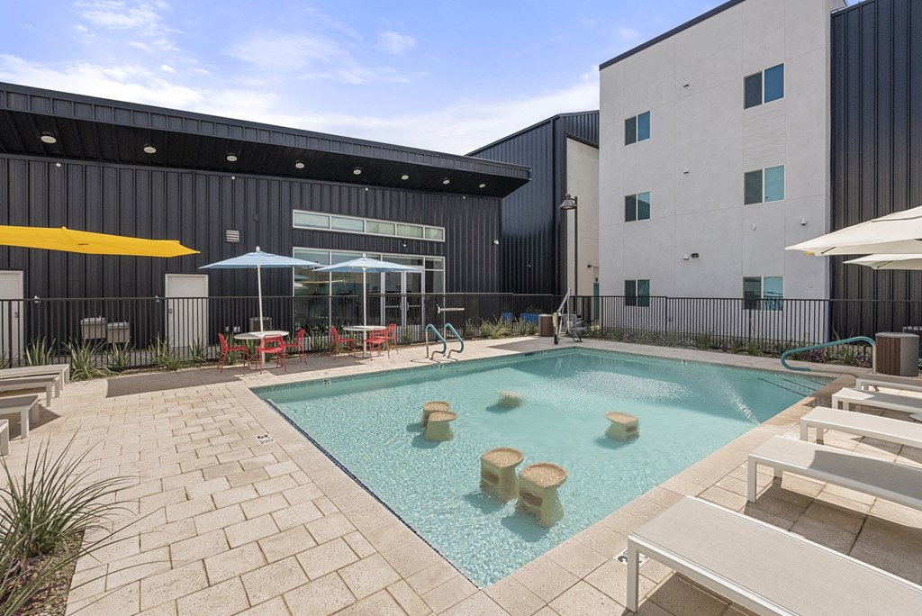 a swimming pool with tables and umbrellas in front of a building at SECOND AVE COMMONS | BRAND-NEW, Mesa