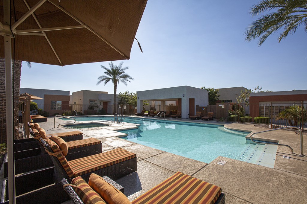 a resort style swimming pool with lounge chairs and umbrellas
