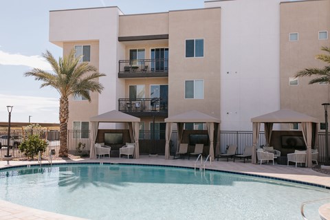 A pool in front of a building with a balcony and chairs.